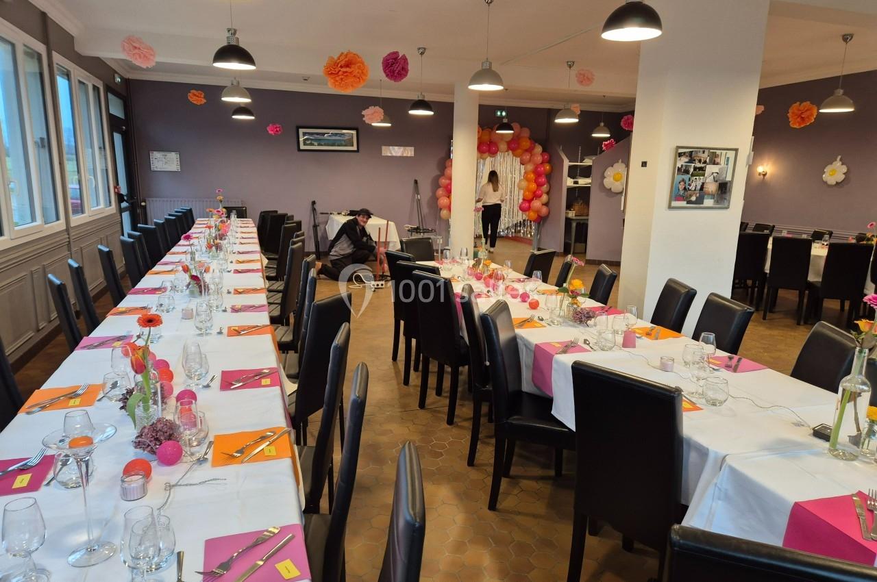 Salle de réception décorée avec des tables dressées, des fleurs colorées et un mur orné de ballons.