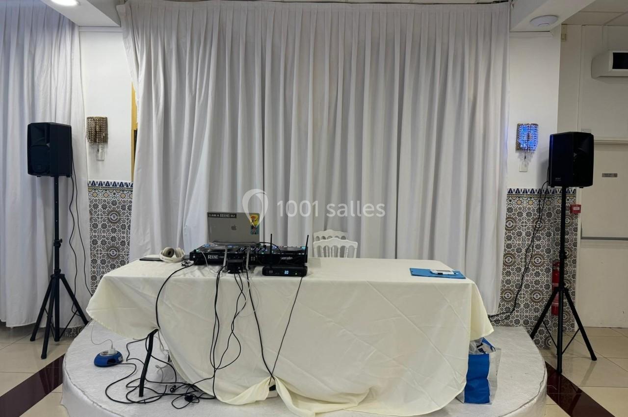 Table recouverte d'une nappe blanche avec matériel audio, câbles et enceintes sur pied dans une salle décorée de rideaux…