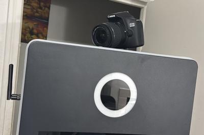 Borne photo équipée d'un appareil photo reflex et d'un anneau lumineux, placée devant une porte entrouverte.