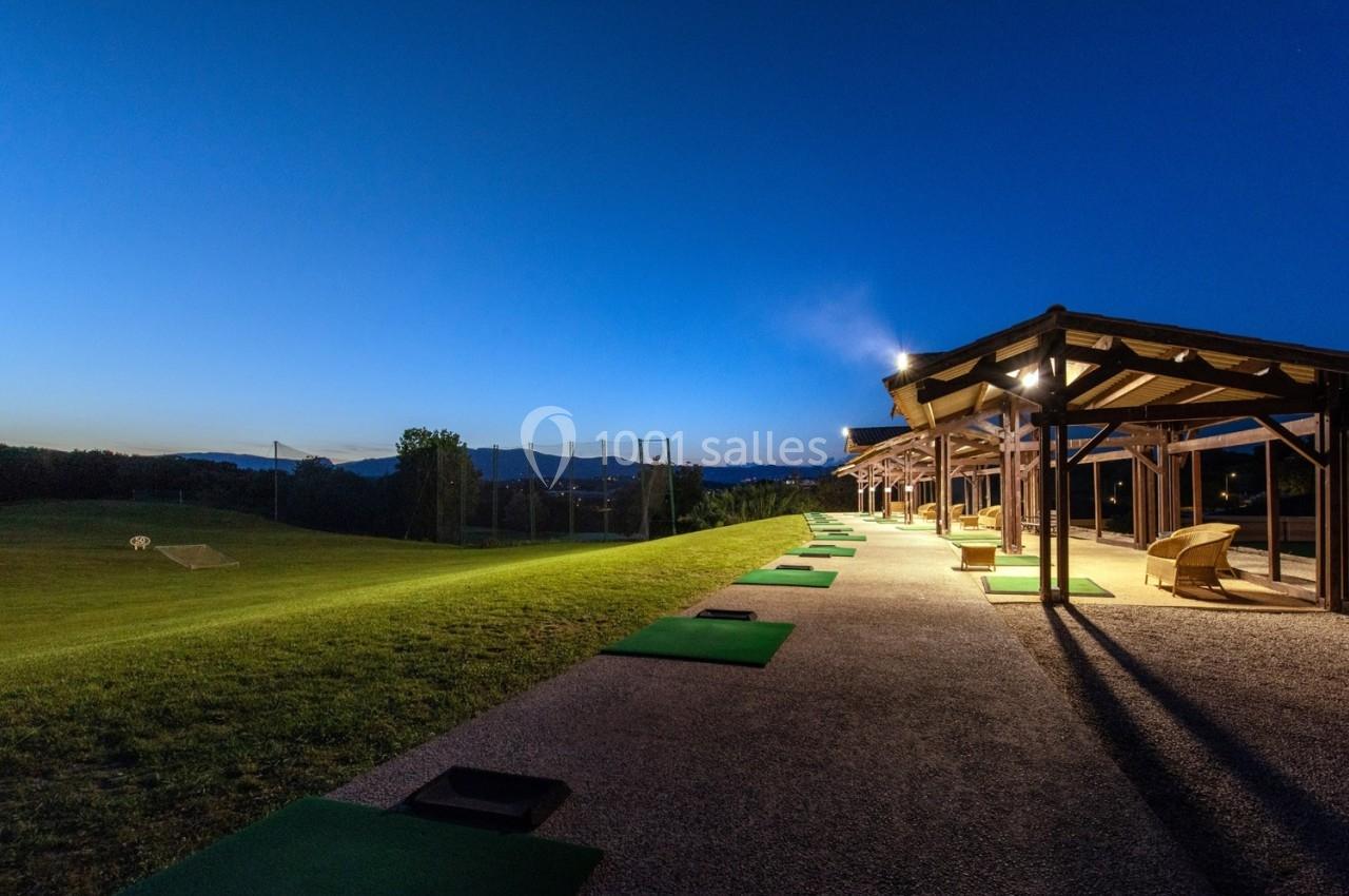 Postes de practice de golf éclairés au crépuscule, avec vue sur un terrain ouvert et des filets de protection.