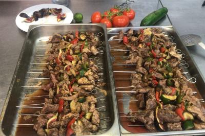 Miniature Traiteur Villecresnes (Val-de-Marne) - Clerence Traiteur #17 Brochettes de viande et légumes colorés disposées sur des plateaux en cuisine, avec des légumes frais en arrière-plan.