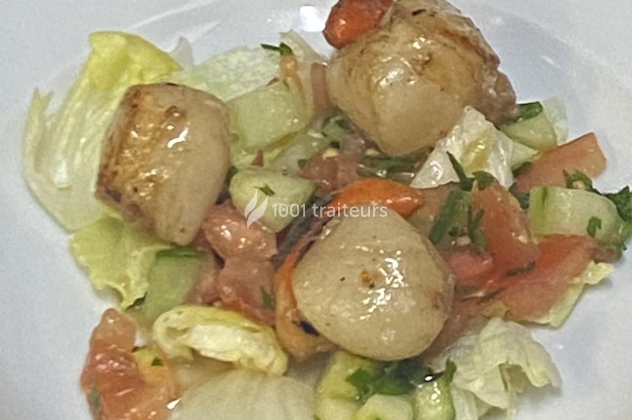 Noix de Saint-Jacques poêlées servies sur un lit de salade verte, tomates et concombres, parsemées de persil.