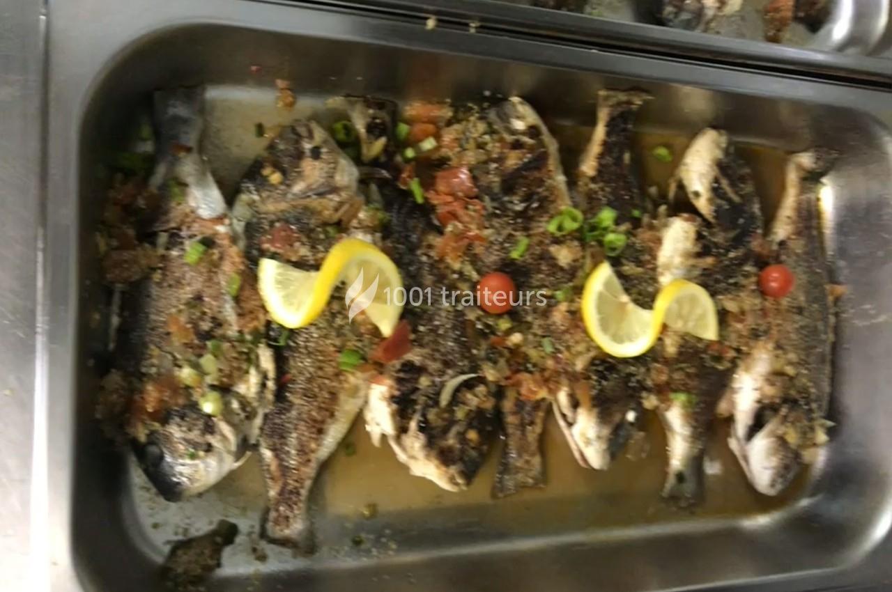 Poissons grillés garnis de rondelles de citron, tomates cerises, herbes et épices, présentés dans un plat en inox.