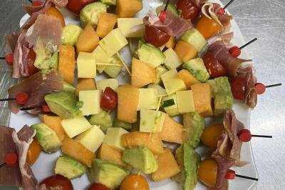 Miniature Traiteur Villecresnes (Val-de-Marne) - Clerence Traiteur #12 Brochettes de viande et légumes colorés disposées sur des plateaux en cuisine, avec des légumes frais en arrière-plan.