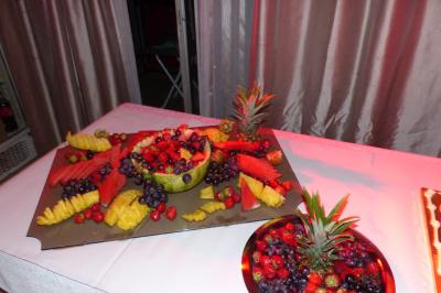 Plateau de fruits variés avec pastèque, ananas, raisins et fraises, disposés sur une table décorée.