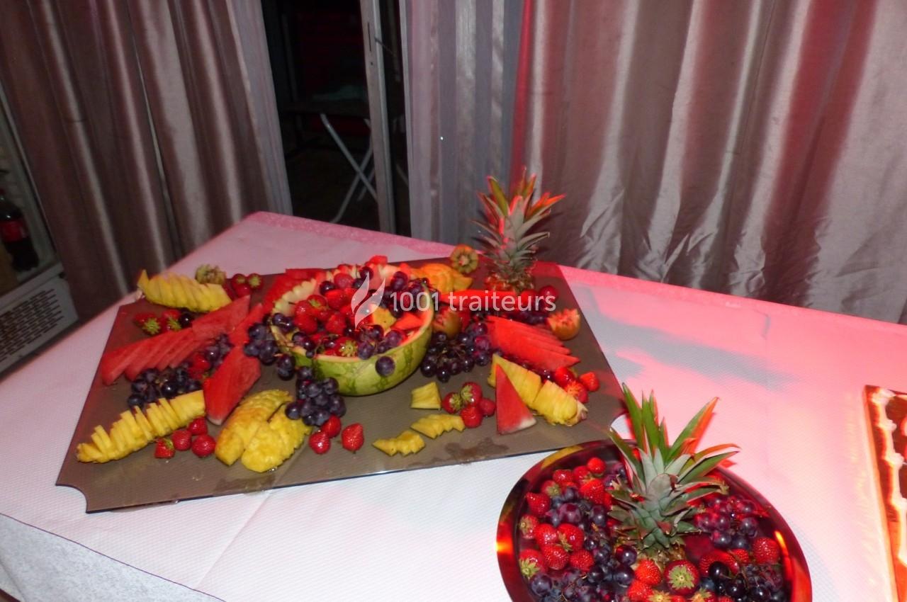 Plateau de fruits variés avec pastèque, ananas, raisins et fraises, disposés sur une table décorée.