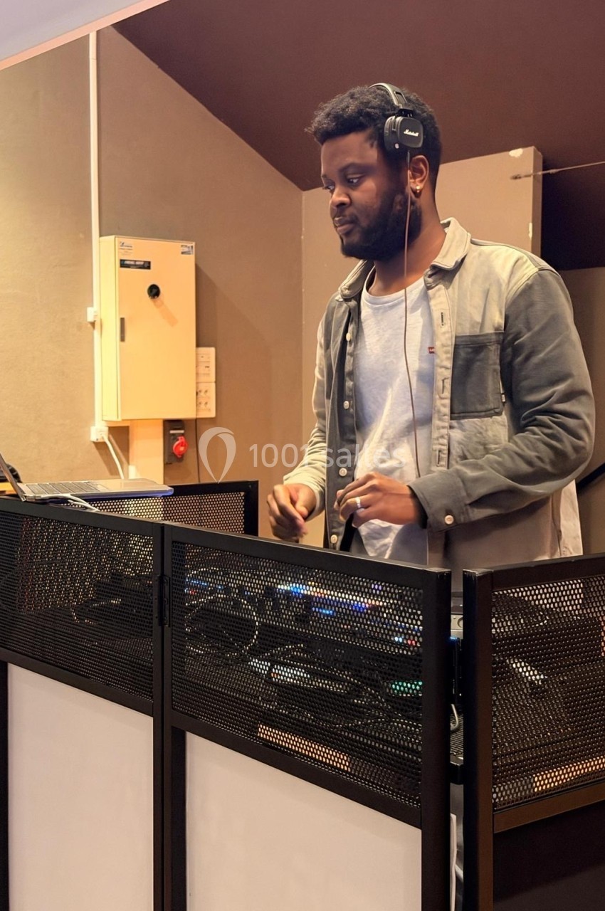 Un DJ mixe de la musique sur une console dans une salle intérieure, portant un casque audio.