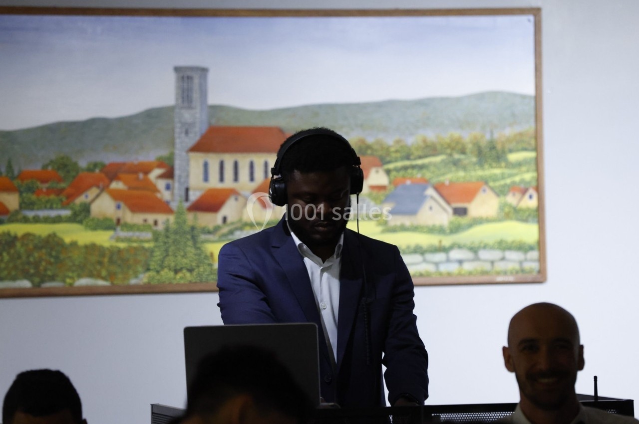 Un DJ en costume mixant de la musique devant un tableau représentant un village avec une église.