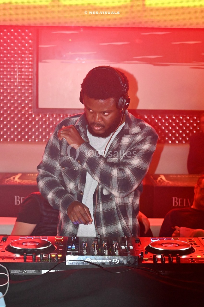 Un DJ concentré mixe de la musique sur une table de mixage dans une ambiance lumineuse rouge.