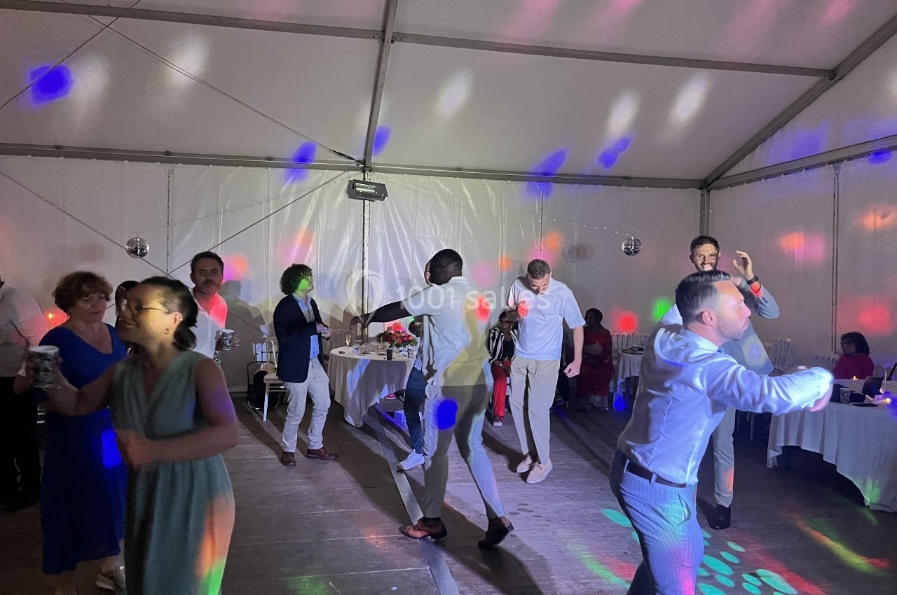 Des personnes dansent sous des lumières colorées dans une grande tente lors d'un événement festif.