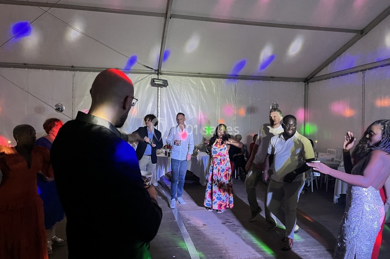 Des personnes dansent sous des lumières colorées dans une salle sous tente lors d'un événement festif.