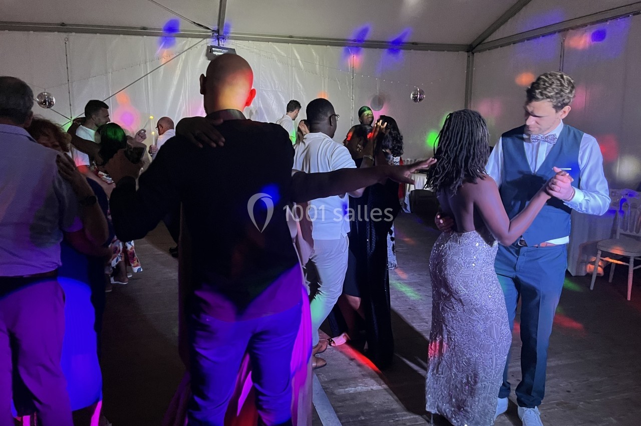 Des personnes dansent sous des lumières colorées dans une salle sous chapiteau lors d'une soirée festive.