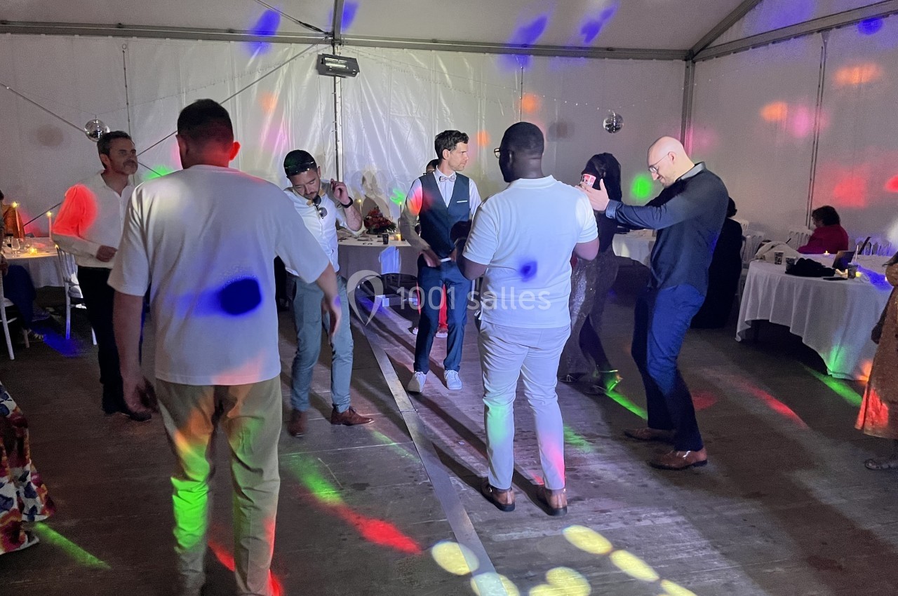 Des personnes dansent sous des lumières colorées dans une salle éclairée, avec des tables en arrière-plan.