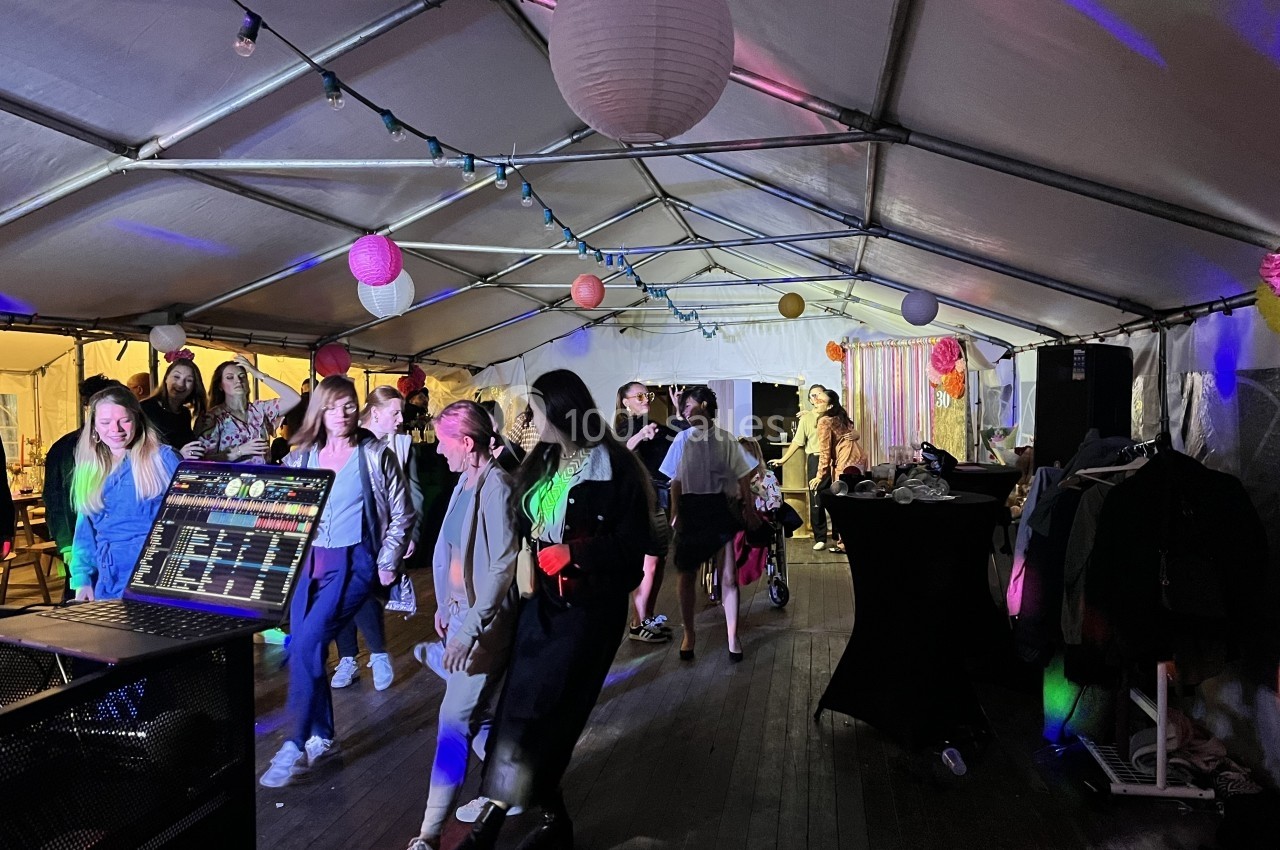 Des personnes dansent sous une tente éclairée par des lumières colorées, avec une table de mixage au premier plan.