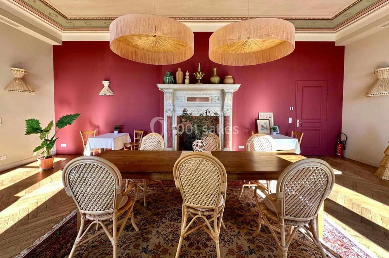 Location salle La Londe-les-Maures (Var) - Château de la Pascalette #3 Salle à manger avec table en bois, chaises en rotin, cheminée décorative et murs rouges.