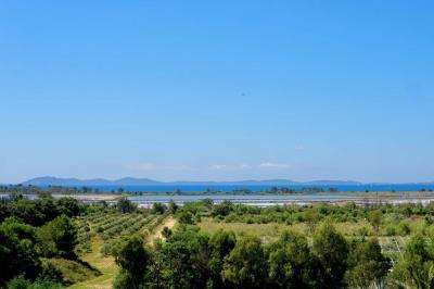 Miniature Location salle La Londe-les-Maures (Var) - Château de la Pascalette #6 Paysage avec des champs verdoyants, des arbres, un lac en arrière-plan et des collines sous un ciel bleu dégagé.