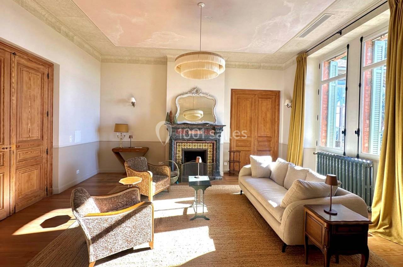 Location salle La Londe-les-Maures (Var) - Château de la Pascalette #5 Salon lumineux avec cheminée décorative, mobilier élégant, grandes fenêtres et parquet en bois clair.