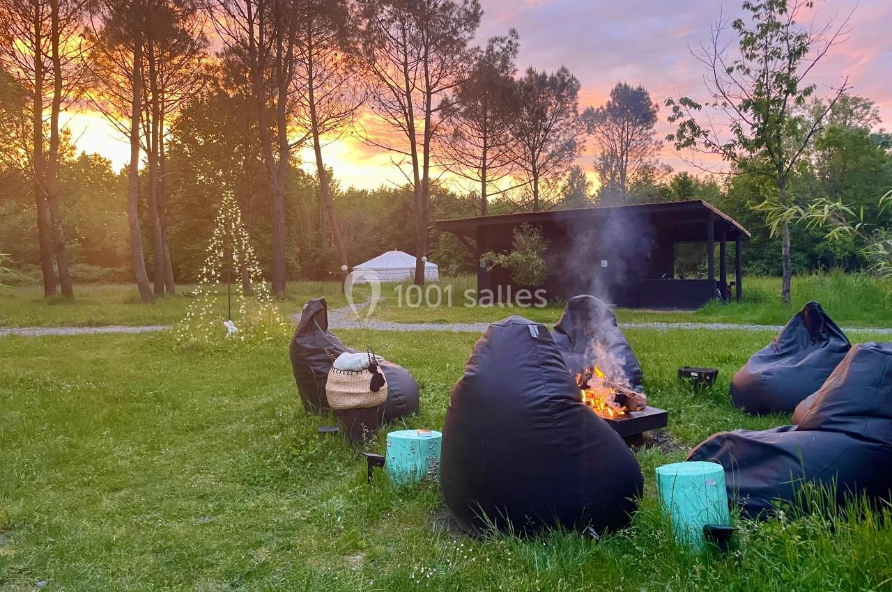 Des fauteuils en toile entourent un feu de camp dans un jardin verdoyant au coucher du soleil.