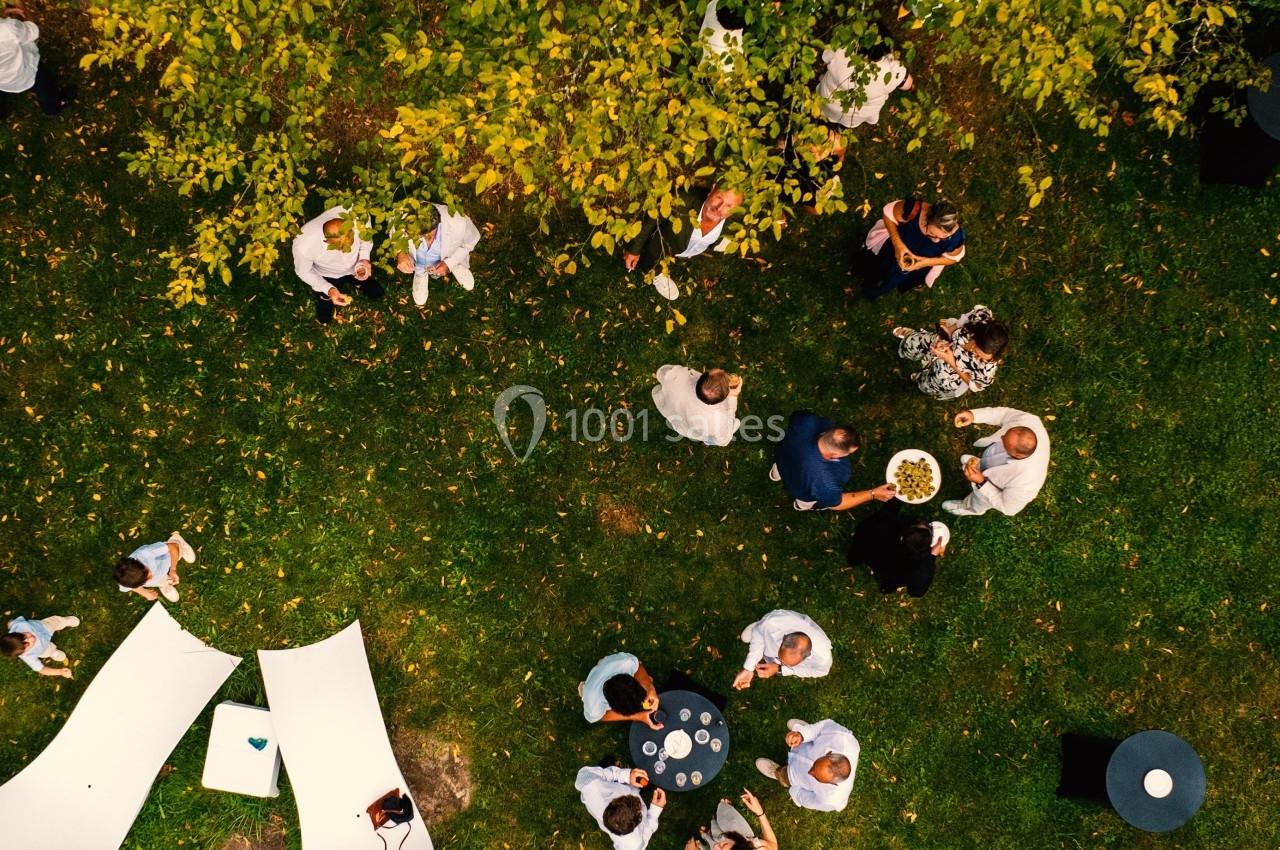 Vue aérienne d'un groupe de personnes discutant et partageant un repas dans un jardin verdoyant.