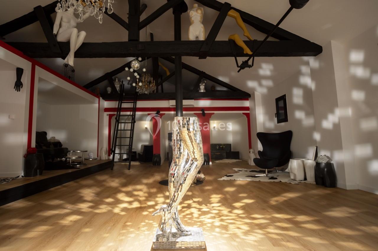 Intérieur d'un loft avec poutres apparentes, sculptures artistiques et lumière réfléchie par une mosaïque.