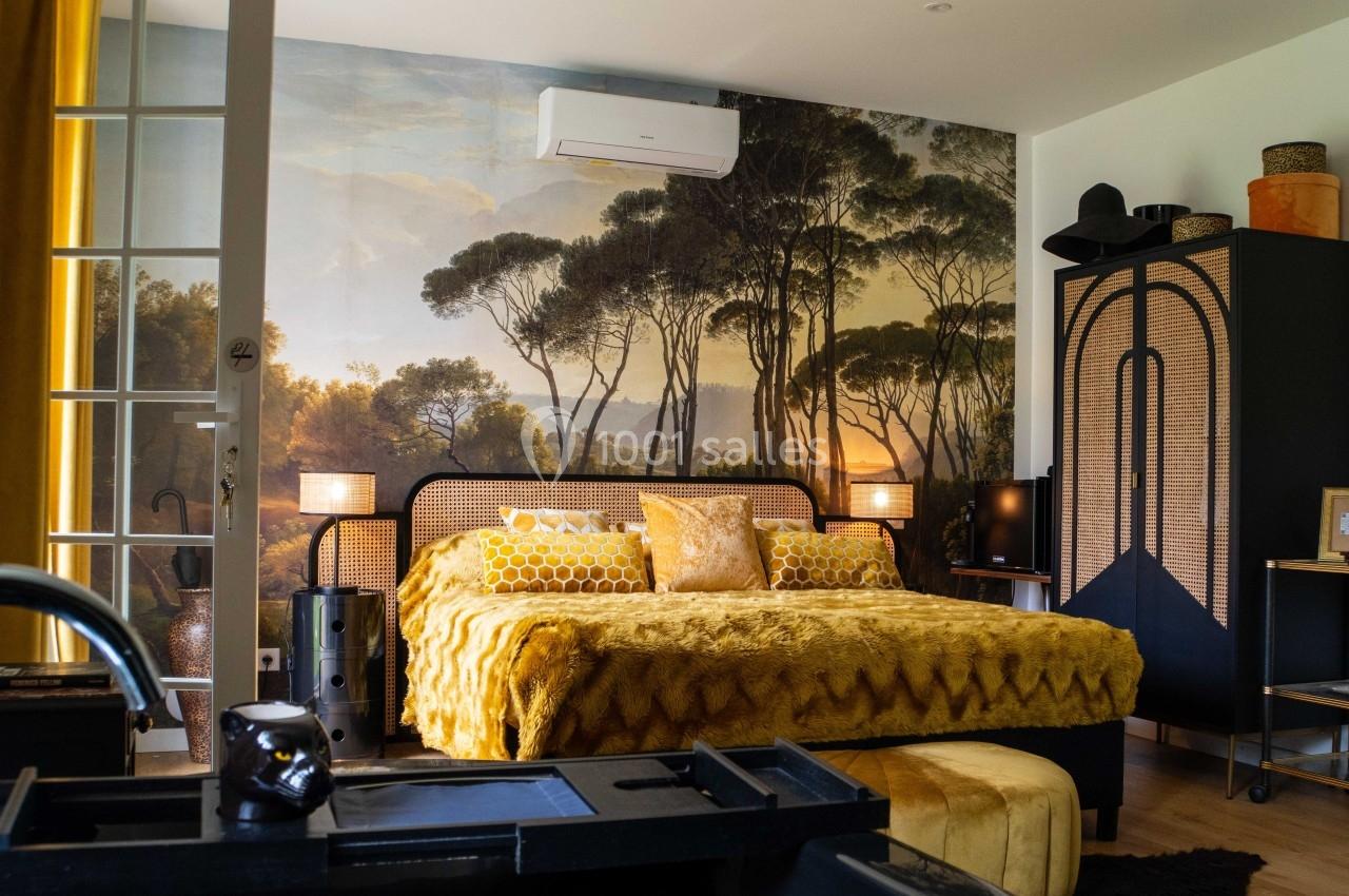 Chambre décorée avec un lit jaune, une fresque murale de paysage boisé, et des meubles en bois et rotin.