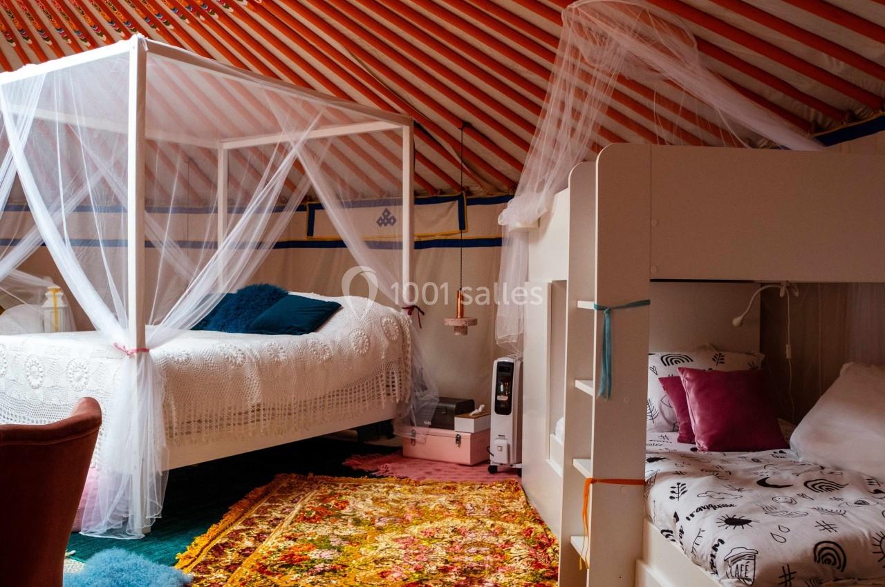 Intérieur d'une yourte aménagée avec un lit à baldaquin, un lit superposé et une décoration chaleureuse.