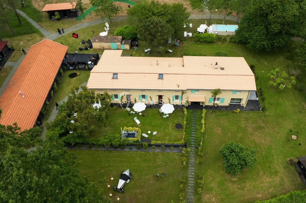 Vue aérienne d'un bâtiment entouré de jardins, avec des tables et parasols installés sur la pelouse.