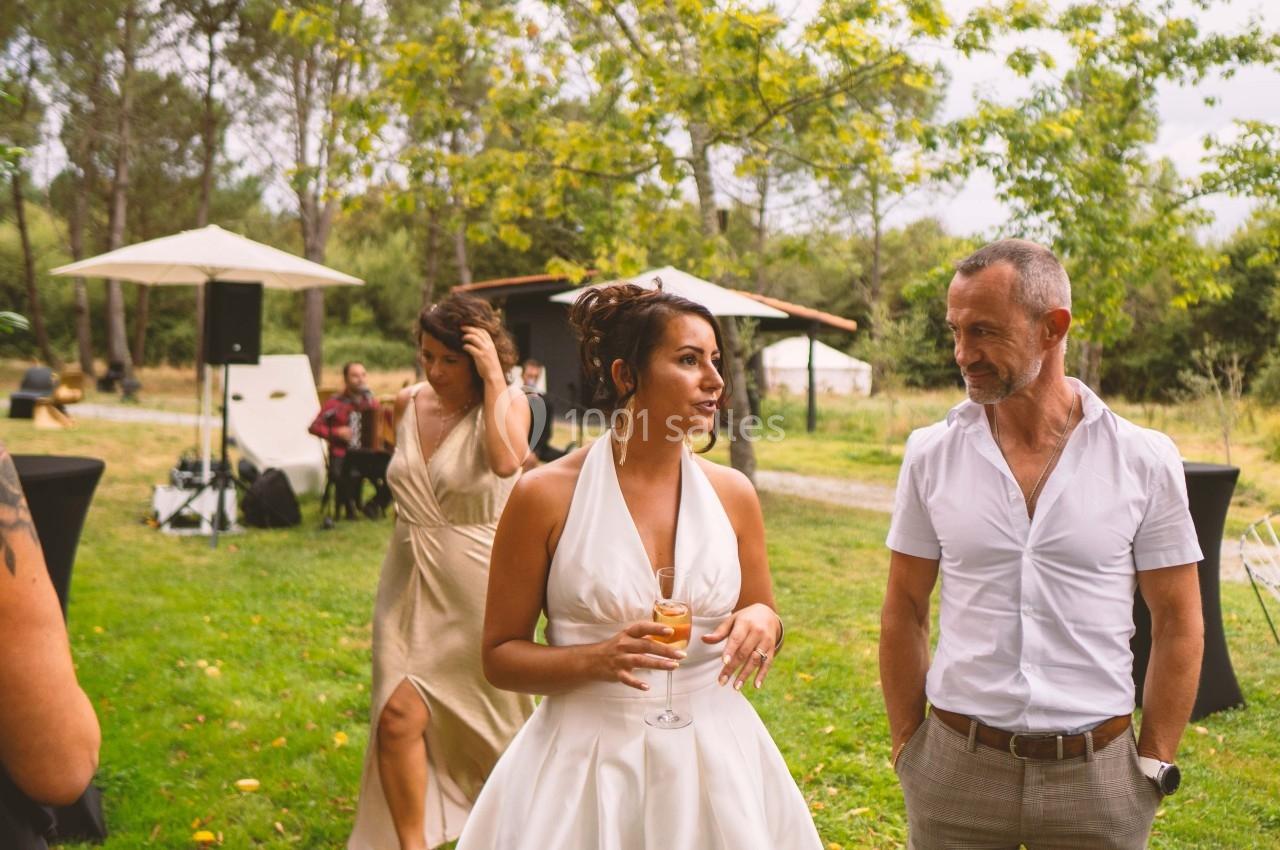 Une femme en robe blanche discute avec un homme en chemise dans un jardin lors d'un événement en plein air.