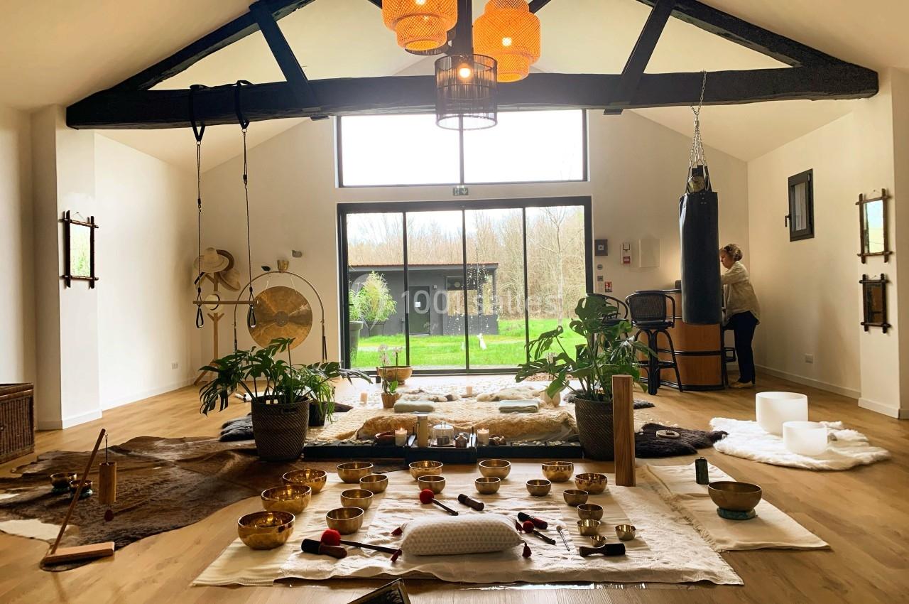 Salle lumineuse avec instruments de relaxation, tapis au sol et vue sur un jardin à travers une grande baie vitrée.