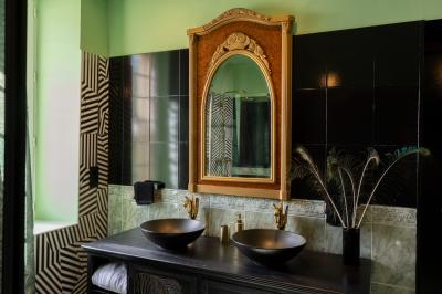 Salle de bain avec un grand miroir doré, deux vasques noires, robinetterie dorée et décoration moderne.