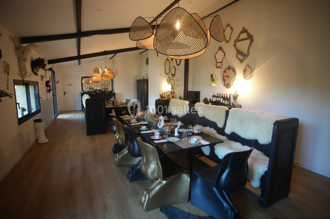 Salle à manger moderne avec table dressée, chaises design noires et dorées, miroirs décoratifs et éclairage suspendu.