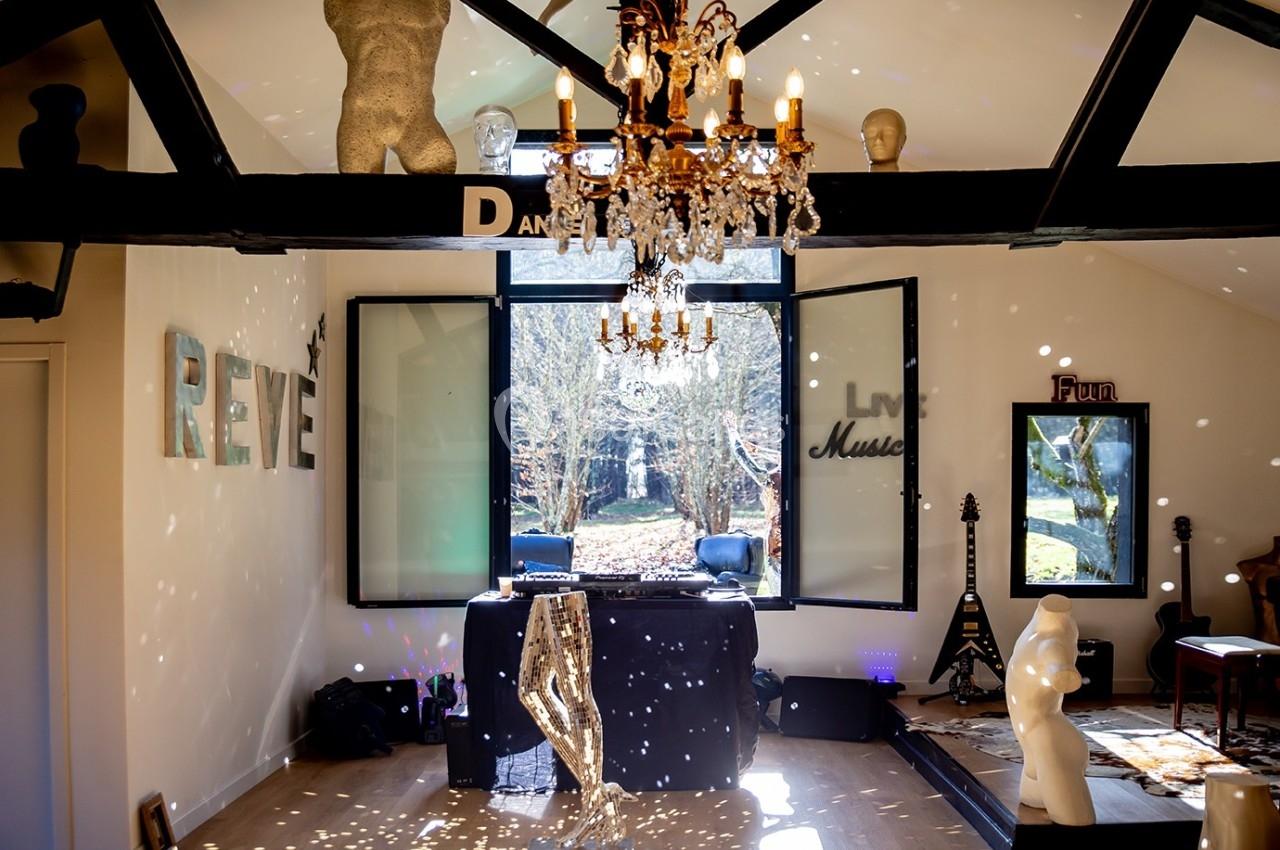 Salle lumineuse avec une grande fenêtre ouverte sur un jardin, décorée d'objets artistiques et d'un lustre.