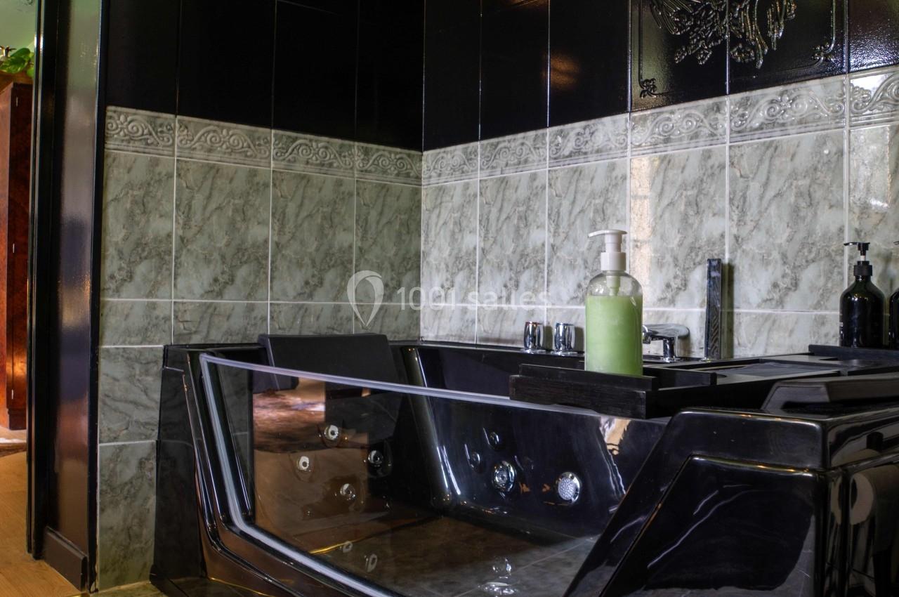 Baignoire noire moderne avec jets intégrés, entourée de carrelage gris et noir dans une salle de bain élégante.