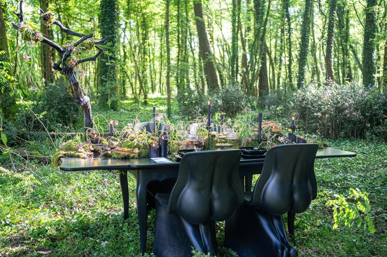 Table décorée avec des éléments naturels et bougies, placée dans une clairière boisée, entourée de végétation dense.
