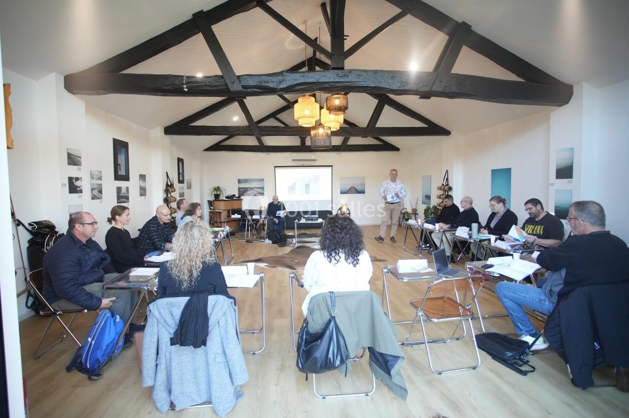 Un groupe de personnes assises en cercle dans une salle avec poutres apparentes, participant à une réunion ou formation.