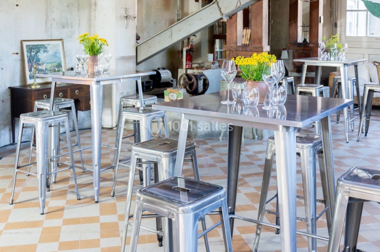Salle lumineuse avec tables et tabourets en métal, décorée de bouquets de fleurs jaunes sur un sol à carreaux.