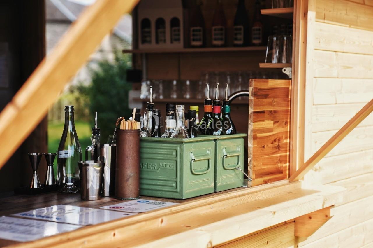 Comptoir en bois avec bouteilles, verres et accessoires de bar disposés à l'intérieur d'une structure ouverte.