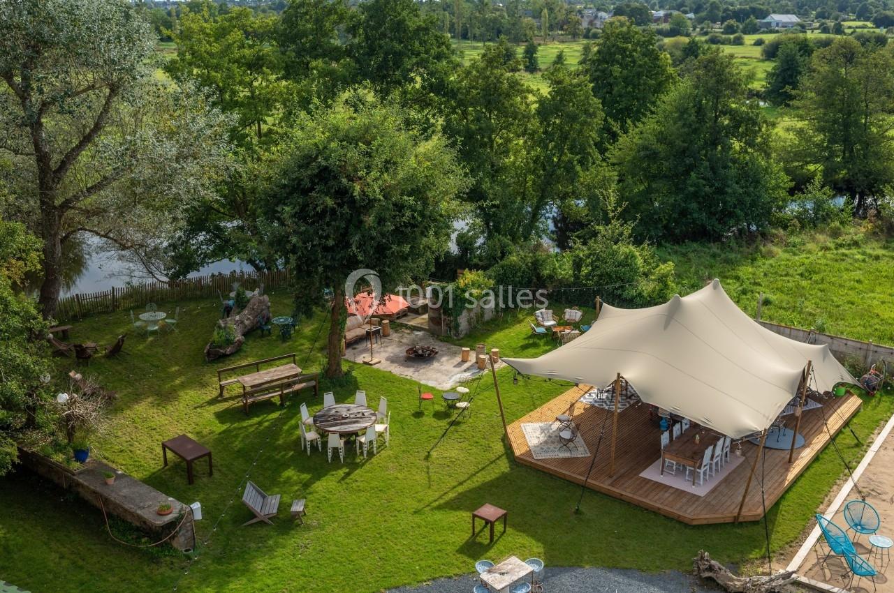 Vue aérienne d'un espace extérieur aménagé avec une tente, des tables, des chaises et un feu de camp près d'une rivière.