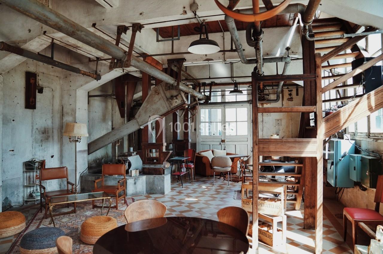 Intérieur d'un loft industriel avec des meubles vintage, des tuyaux apparents et un éclairage naturel.