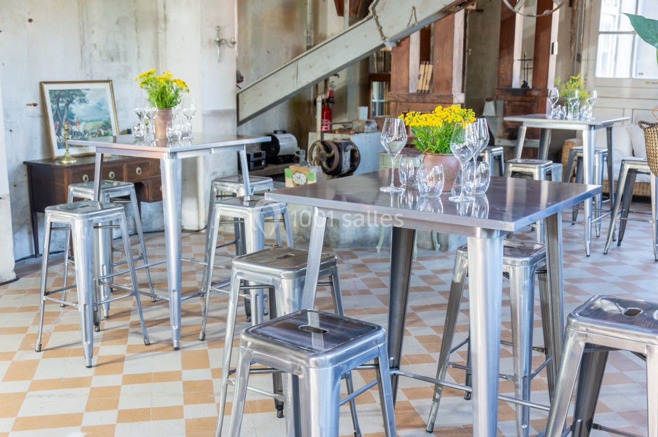 Salle lumineuse avec tables et tabourets en métal, décorée de bouquets de fleurs jaunes et éléments rustiques en arrière…