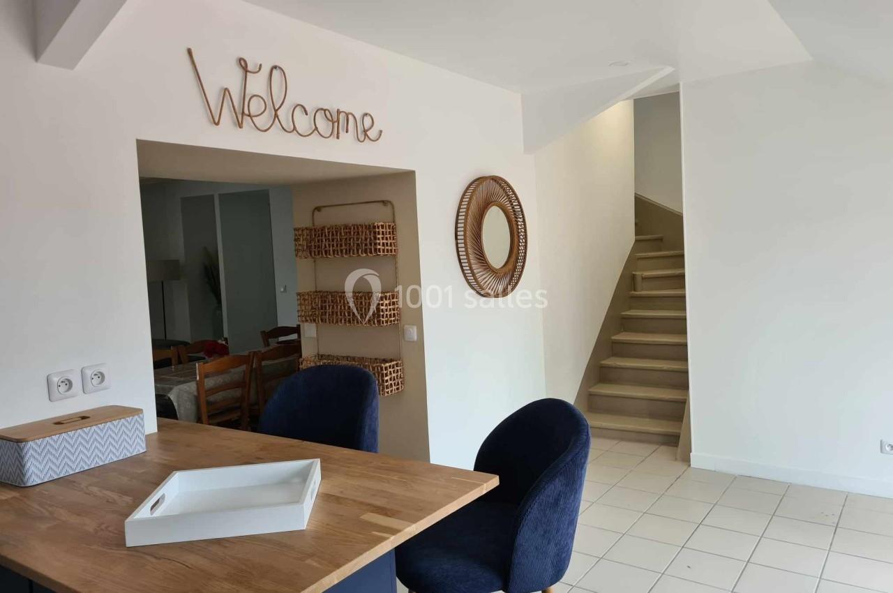 Cuisine ouverte avec un plan de travail en bois, deux chaises, un escalier et une décoration murale ’Welcome’.