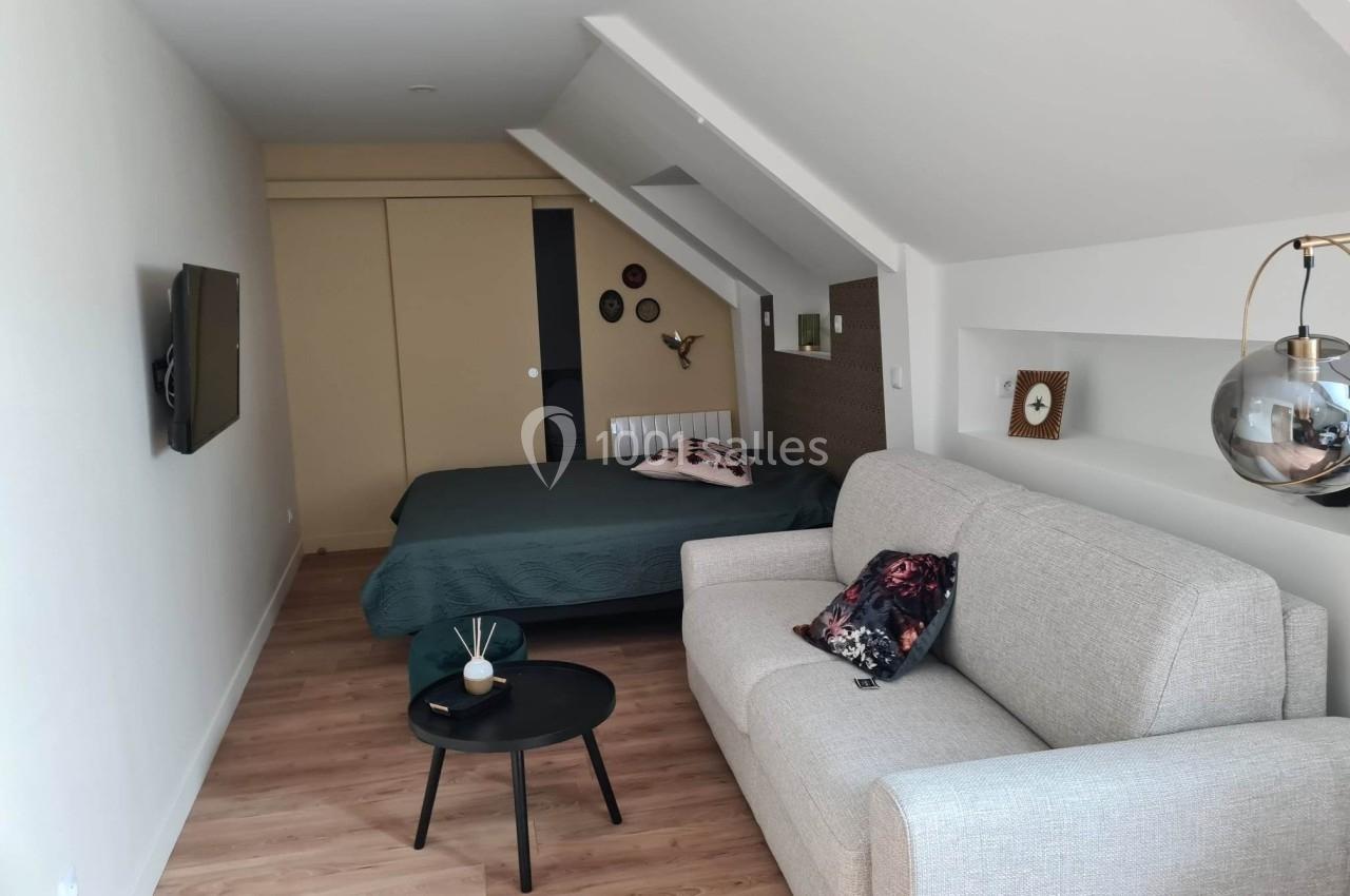 Studio mansardé avec un lit double, un canapé, une table basse, une télévision murale et un éclairage moderne.