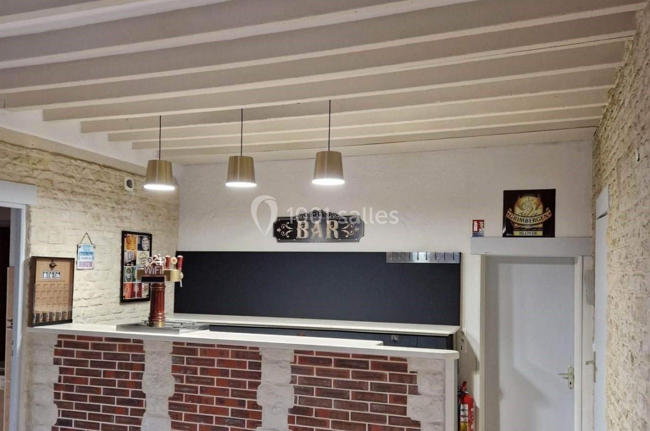 Comptoir de bar en briques avec trois suspensions au plafond, entouré de murs en pierre et d'une porte blanche.