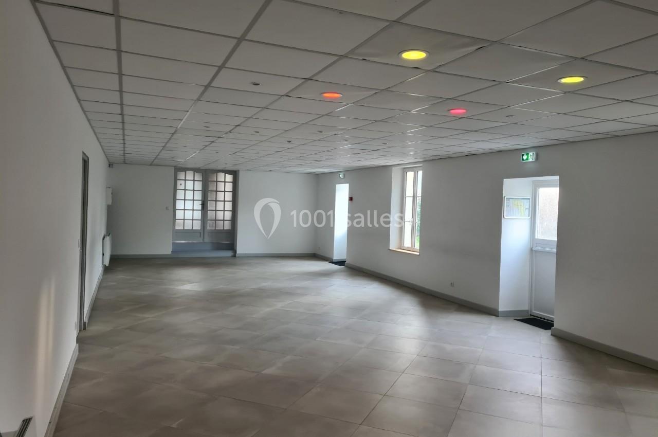Salle vide avec carrelage clair, plafond à dalles blanches et quelques spots lumineux colorés.