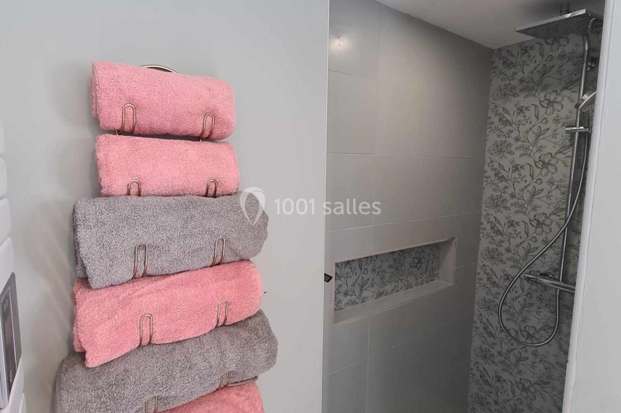 Salle de bain moderne avec douche à l'italienne, mur à motif floral et serviettes pliées sur un porte-serviettes.