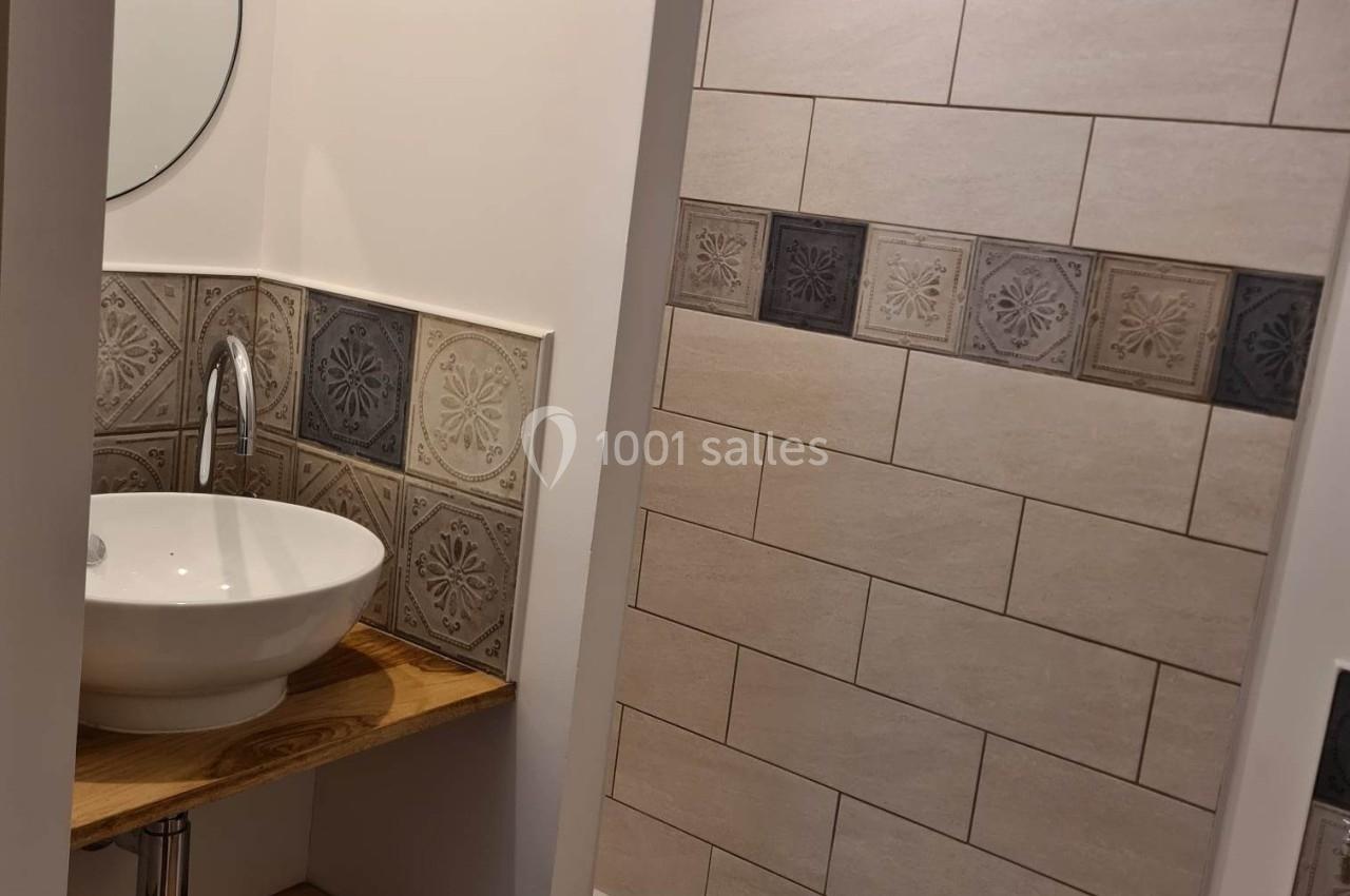 Salle de bain moderne avec lavabo sur étagère en bois, miroir rond et douche à carrelage beige et décoratif.