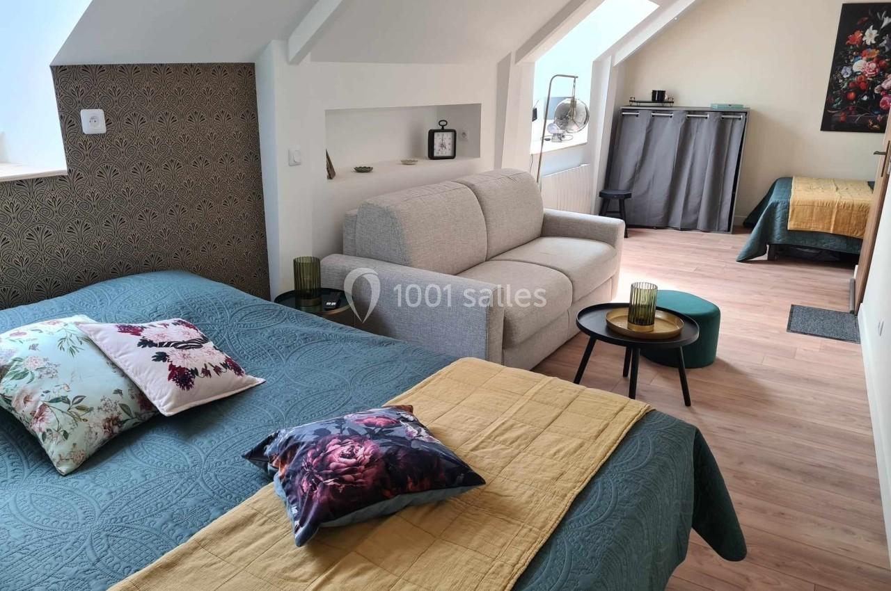 Chambre lumineuse avec lit double, canapé, table basse, et lit simple en arrière-plan, décorée avec des tons chaleureux.
