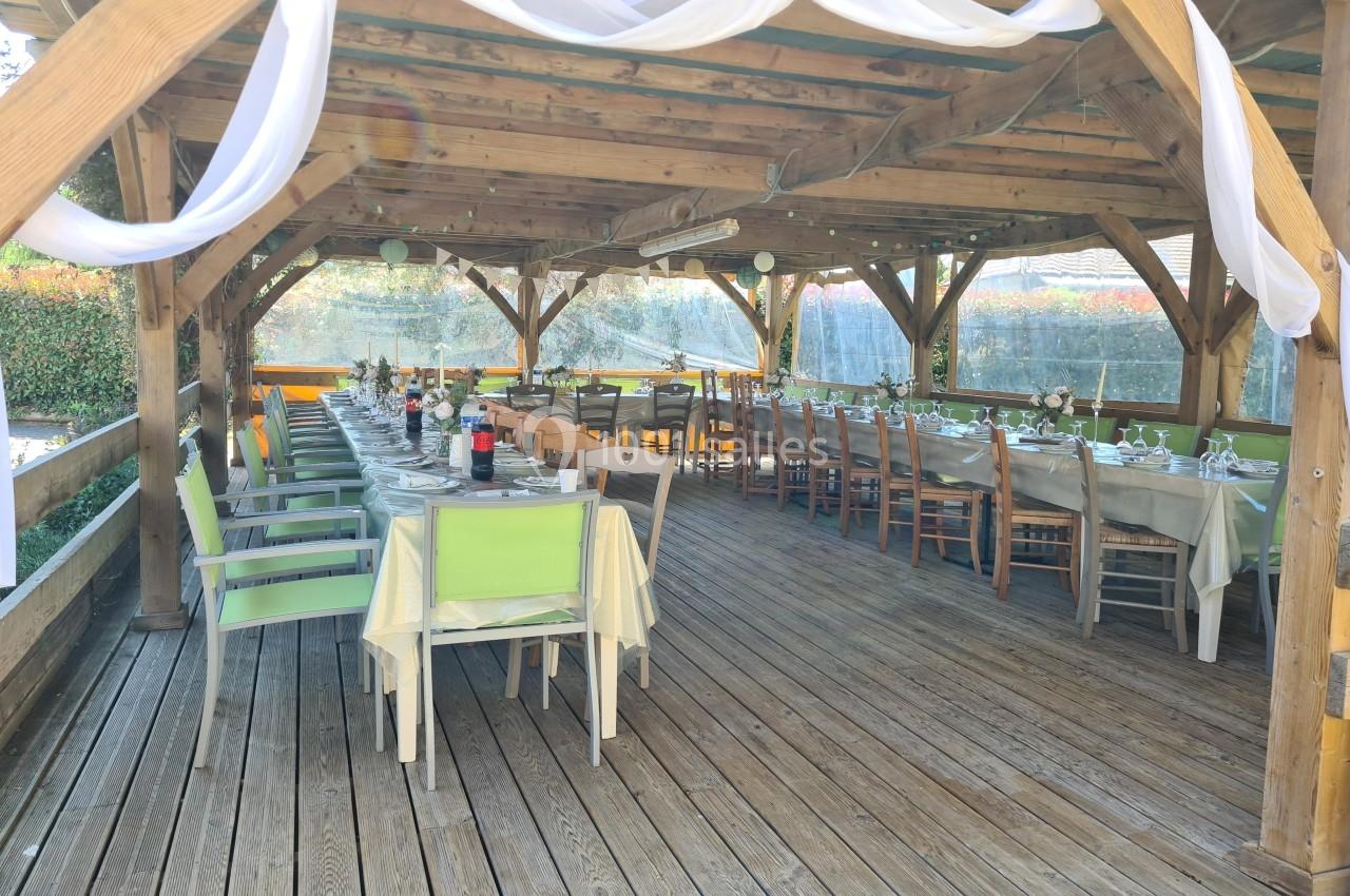Tables dressées sous une pergola en bois, décorée de voilages blancs, dans un cadre extérieur ensoleillé.