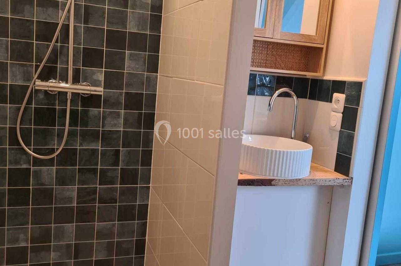 Douche à l'italienne avec carrelage sombre à gauche et lavabo blanc sur meuble en bois à droite.