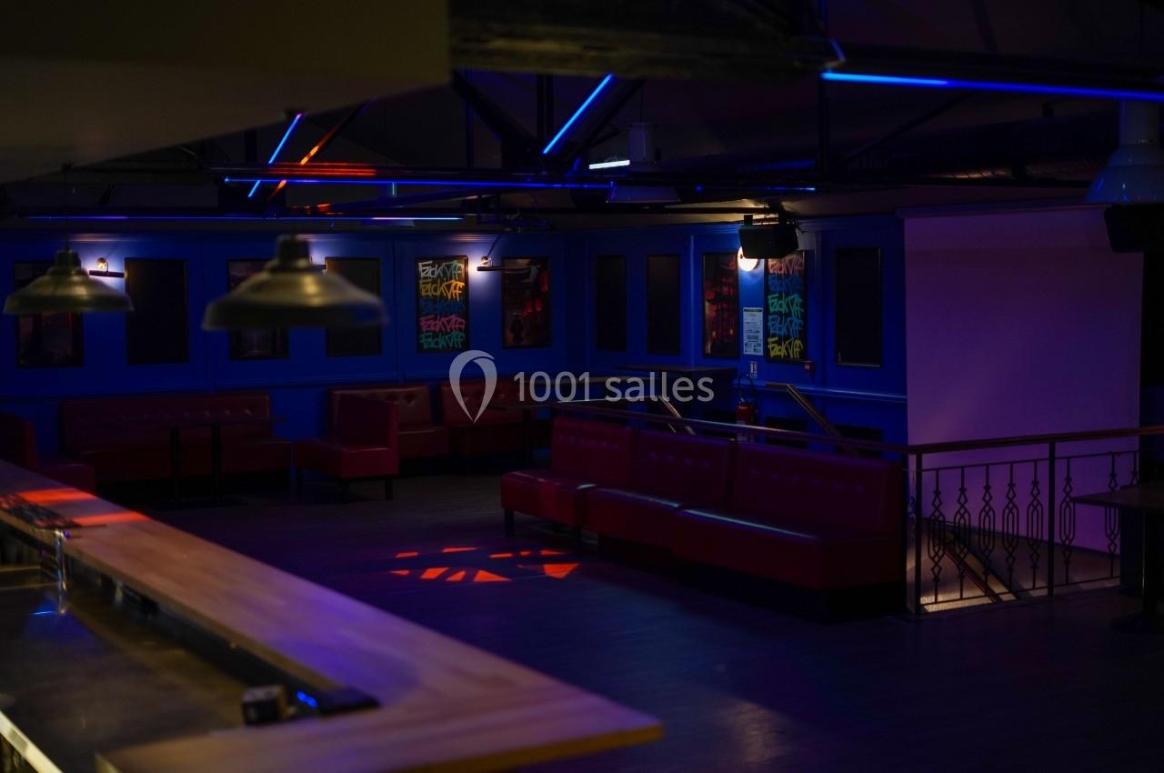 Salle de bar sombre avec banquettes rouges, éclairage tamisé et néons colorés sur les murs.